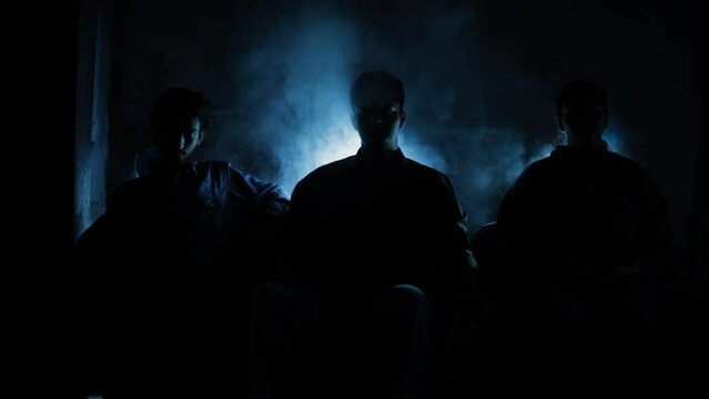 Film-like footage of three people sitting on a couch in a dark smoky environment, HD stock footage.