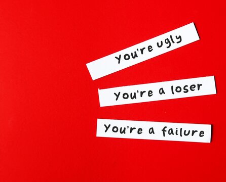 On copy space red background, paper written You're ugly , You're a loser, You're a failure - verbal abuse  - negative demeaning words abuser uses to gain or maintain power and control over victim