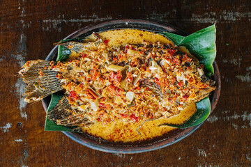 Deep-fried gourami with sweet and sour sauce on a wooden plate. Gurame Asam Manis. Flat lay or top view.