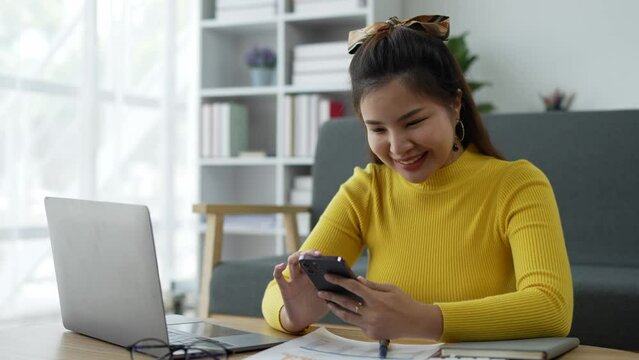 Happy and relaxed Asian woman using a smartphone to send text messages, chat online, and view wireless internet on the device. Shopping online from home.