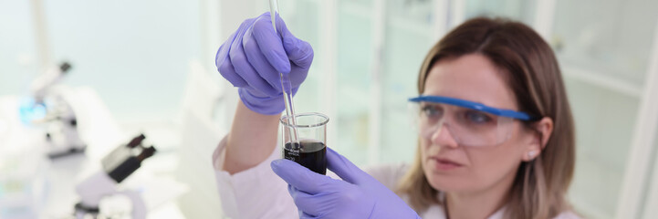 Focused scientist in goggles mixes black liquid in glassware