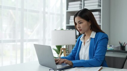 Asian businesswoman, self-employed working on a laptop computer typing e-commerce marketing financial report on real estate project in office management concept.