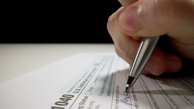 Closeup macro shot movement shot of corporate accountant or individual tax payer filling out 1040 tax form with name and personal information preparing for tax season and submitting financial report.