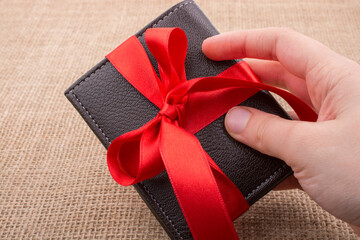 Hand holding a wallet wrapped with ribbon - obrazy, fototapety, plakaty
