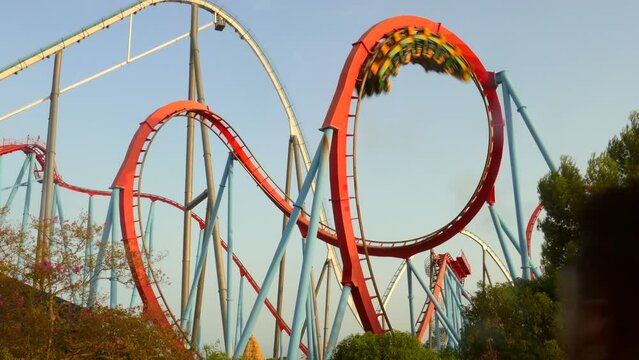 Low angle shot of cobra roll in dragon rollercoaster inside Port Aventura amusement park in Salou, Spain during evening time. 4K.