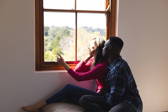 Diverse couple embracing and looking through window at home