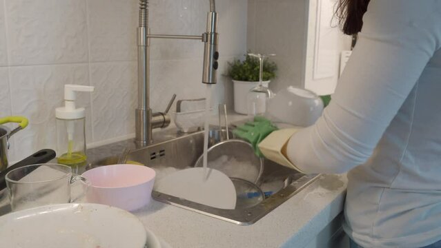 woman washing pile of dirty dishes in the kitchen sink at home
