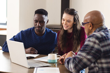 Diverse couple and biracial male financial advisor using laptop and discussing documents at home