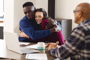 Diverse couple and biracial male financial advisor using laptop and discussing documents at home