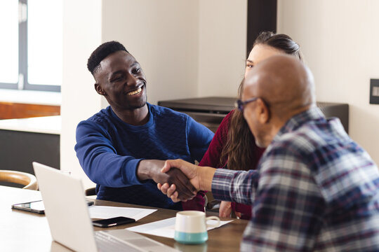Diverse couple and biracial male financial advisor using laptop and shaking hands at home