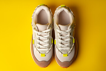 Beige sport running shoes on yellow studio background - obrazy, fototapety, plakaty