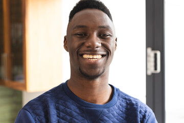 Portrait of happy african american man wearing blue jumper smiling in kitchen at home
