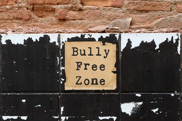 Old vintage ruined brick grunge cracked tiled wall background with text on paper BULLY FREE ZONE,...