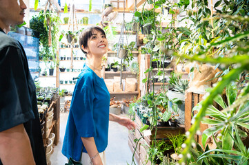 A stylish Asian man and woman couple happily shop for houseplants in a plant shop. Environmental considerations. Sustainability.Seasonal shopping.
