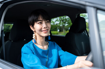 Portrait of a beautiful smiling young Asian woman sitting in her car, looking out of the window and smiling. Driving in the city. On the move. Car rental. Car insurance.