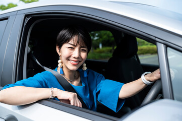 Portrait of a beautiful smiling young Asian woman sitting in her car, looking out of the window and...