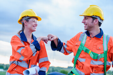 Fist bump of Architectural Engineering Caucasian working and maintenance with wind turbine blueprint pictures of wind turbines at windmill field farm. Alternative renewable energy for better living