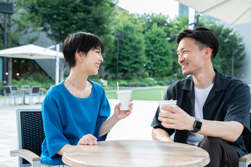 Beautiful woman smiling and talking to man. Park with lots of greenery. Chatting on a café terrace...