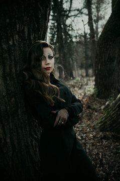 A young woman in a Gothic gloomy image of a witch in a forest surrounded by smoke. Halloween costume. Vertical photo.