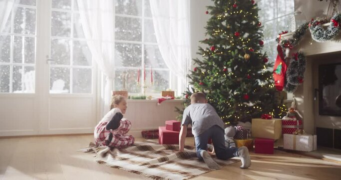Slow Motion of Cute Kids in Pajamas Running To Get Their Gifts On Christmas Bright Morning. Happy Kids Getting Surprised While Opening Holiday Wrapped Gift Boxes, Receiving New Toys from Santa 