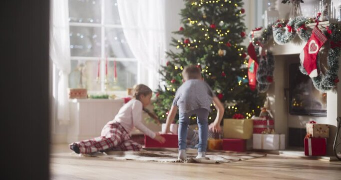 Slow Motion of Happy Little Brother and Sister Waking Up on Holiday Morning to Receive New Toys from Under the Christmas Tree. Cute Children Running Impatiently to Get Their Gifts 
