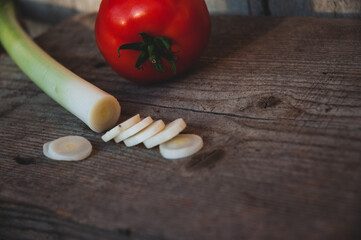 Sliced leek on a wooden chopping board and tomato. Food concept. Flat lay.