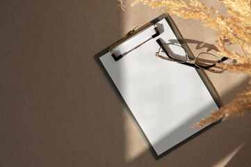 Blank clipboard mockup with paper sheet, eyeglasses, meadow grass and aesthetic natural sunlight...