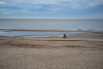 Fototapeta na wymiar very wide empty sandy beach at low tide with bicyclists in the distance