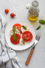Traditional Italian caprice salad of mozzarella, tomatoes, basil and olive oil, served on a light background.