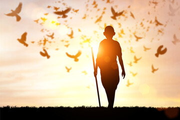 silhouette of a person walking with stick under the sun, with pigeons flying around him for Gandhi jayanti holiday celebration on the 2nd of october