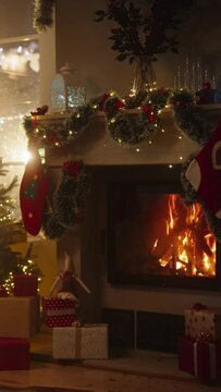 Vertical Screen: Warm Atmosphere on a Winter Snowy Night: Empty Shot of Home Interior with Fireplace Decorated with Christmas Tree, Gifts, Ornaments, Garlands and Stockings. Magical Time for Holidays