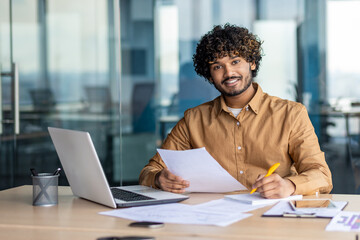 Portrait of young successful Indian businessman, man paper work smiling and looking at camera,...