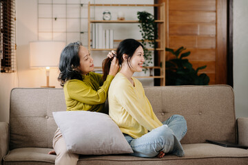 Fototapeta premium Happy adult granddaughter and senior grandmother having fun enjoying talk sit on sofa in living room at home.