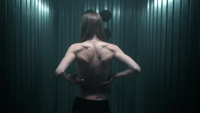 A beautiful slender brunette girl touches her bare back with her hands. Lean skinny female young body in the studio. Muscles, joints and tendons. Fashion video.