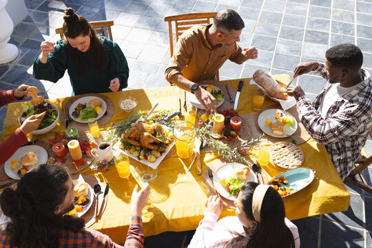 Happy diverse male and female friends eating thanksgiving celebration meal in sunny garden