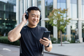Asian young man in sports uniform standing in the middle of the street wearing headphones and...