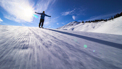 Silhouette of a skier skiing on slopes in the Swiss alps towards the camera. Hands widely spread out.