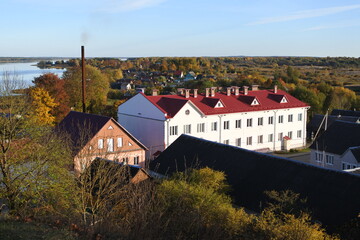 A white two-storey building with a red roof.  Landscape with a small town on the background of a forest. 
