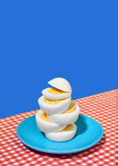 Sliced, hard-boiled eggs on blue plate, on checkered tablecloth over blue background. Concept of breakfast, food, taste, health, creativity. Pop art photography. Poster. Copy space for ad