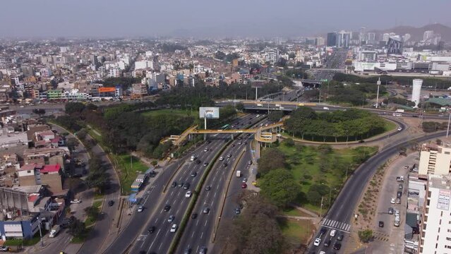 Drone footage of a cloverleaf interchange called "Trebol Javier Prado". Drone flies slowly over the main long street called "Javier Prado".  buildings go on into the distance. Located in Lima, Peru.