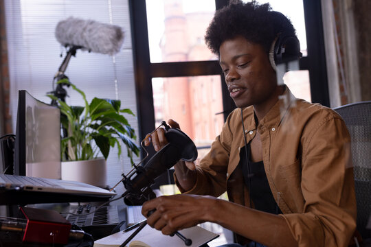 Happy african american man in headphones making live podcast using microphone at home, copy space