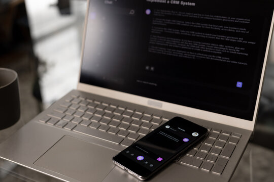 Laptop on desk and smartphone on keyboard with web chat on screen at home office