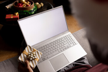African american man at home holding christmas gift having video call on laptop with copy space