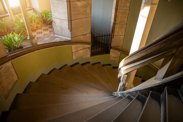 Old castle stone spiral staircase with flower plants on stage floor and sun light in window....