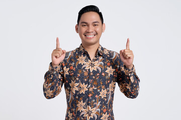 Excited young Asian teacher man 30s wearing batik shirt pointing finger up, having great idea...