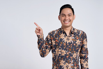 Smiling happy young Asian teacher man wearing batik shirt pointing fingers aside at copy space for...