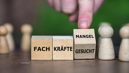 Hand turns wooden cube and changes the German expression 'Fachkraefte gesucht' (skilled workers wanted) to 'Fachkraeftemangel' (skilled workers demand).