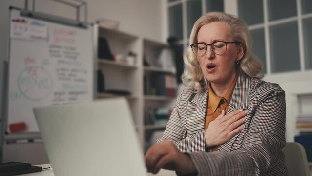 Businesswoman in her 50s feeling strong chest pain while working laptop, spasm
