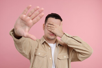 Embarrassed man covering face with hand on pink background