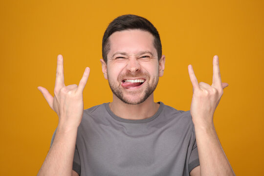 Happy man showing his tongue and rock gesture on orange background